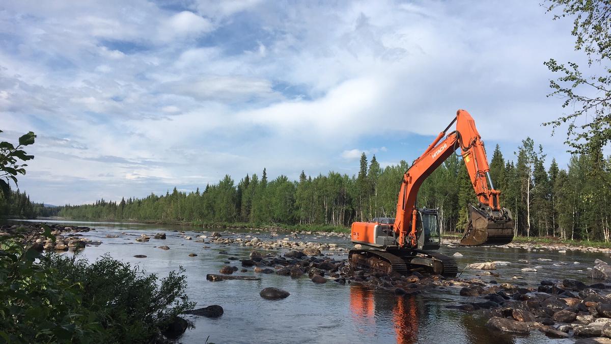 Grävmaskin som lägger tillbaka sten i ett grunt vattendrag